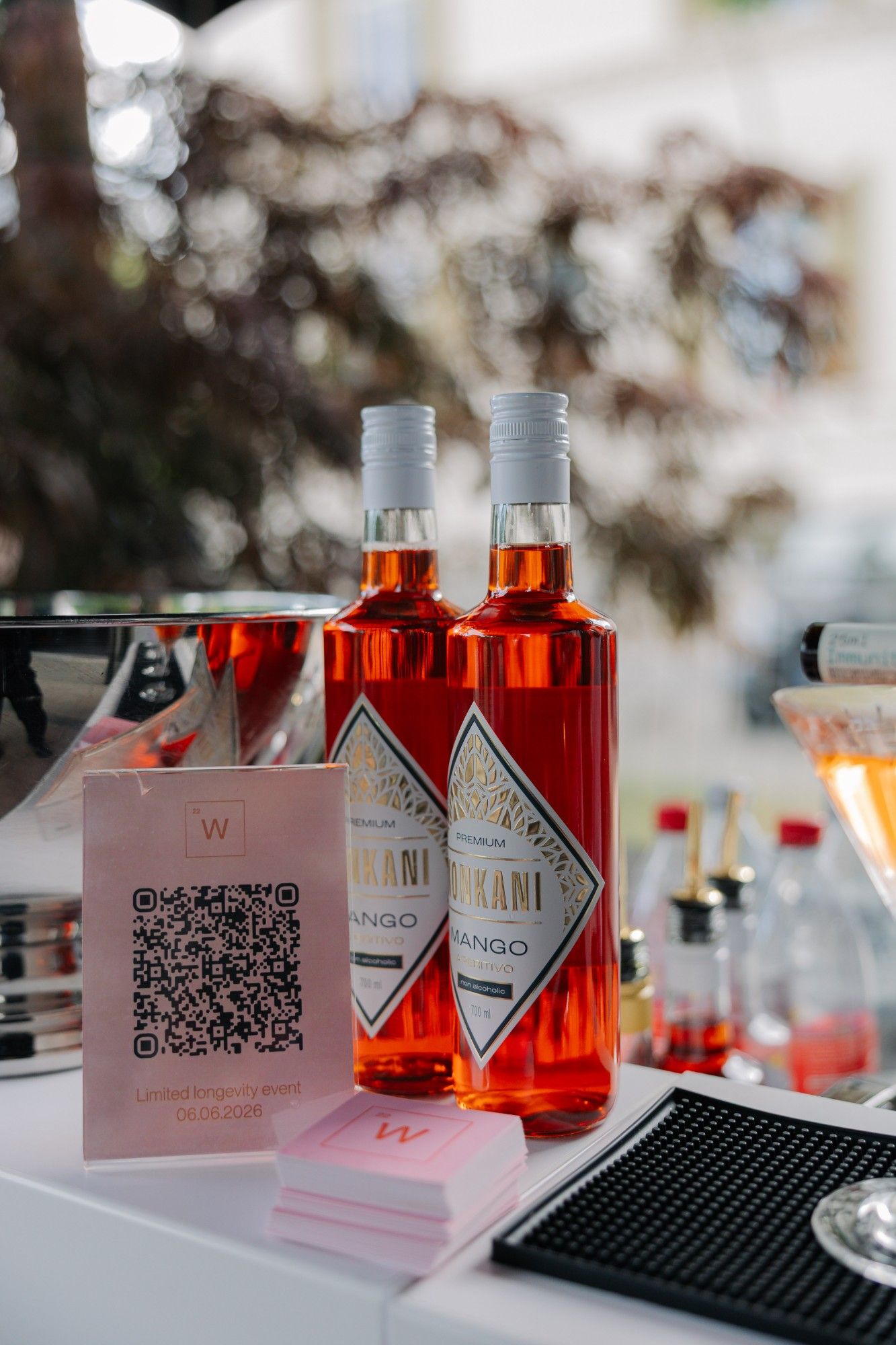Zwei Flaschen alkoholfreier Aperitivo neben einem Aufsteller mit QR-Code.