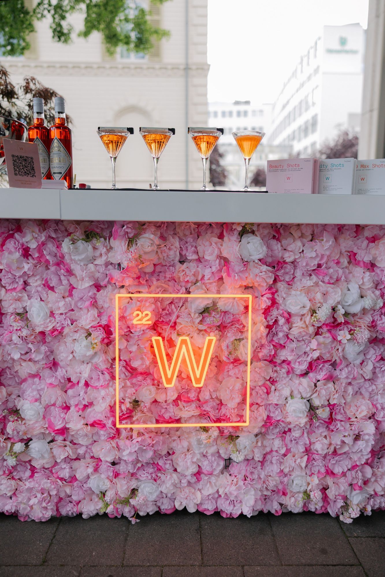 Bar mit Blumenwand, Neon-Logo und Cocktails.