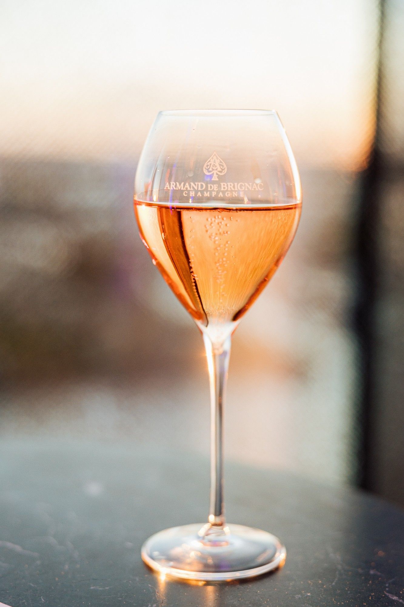 Glas Rosé-Champagner mit Armand-de-Brignac-Gravur im Abendlicht.