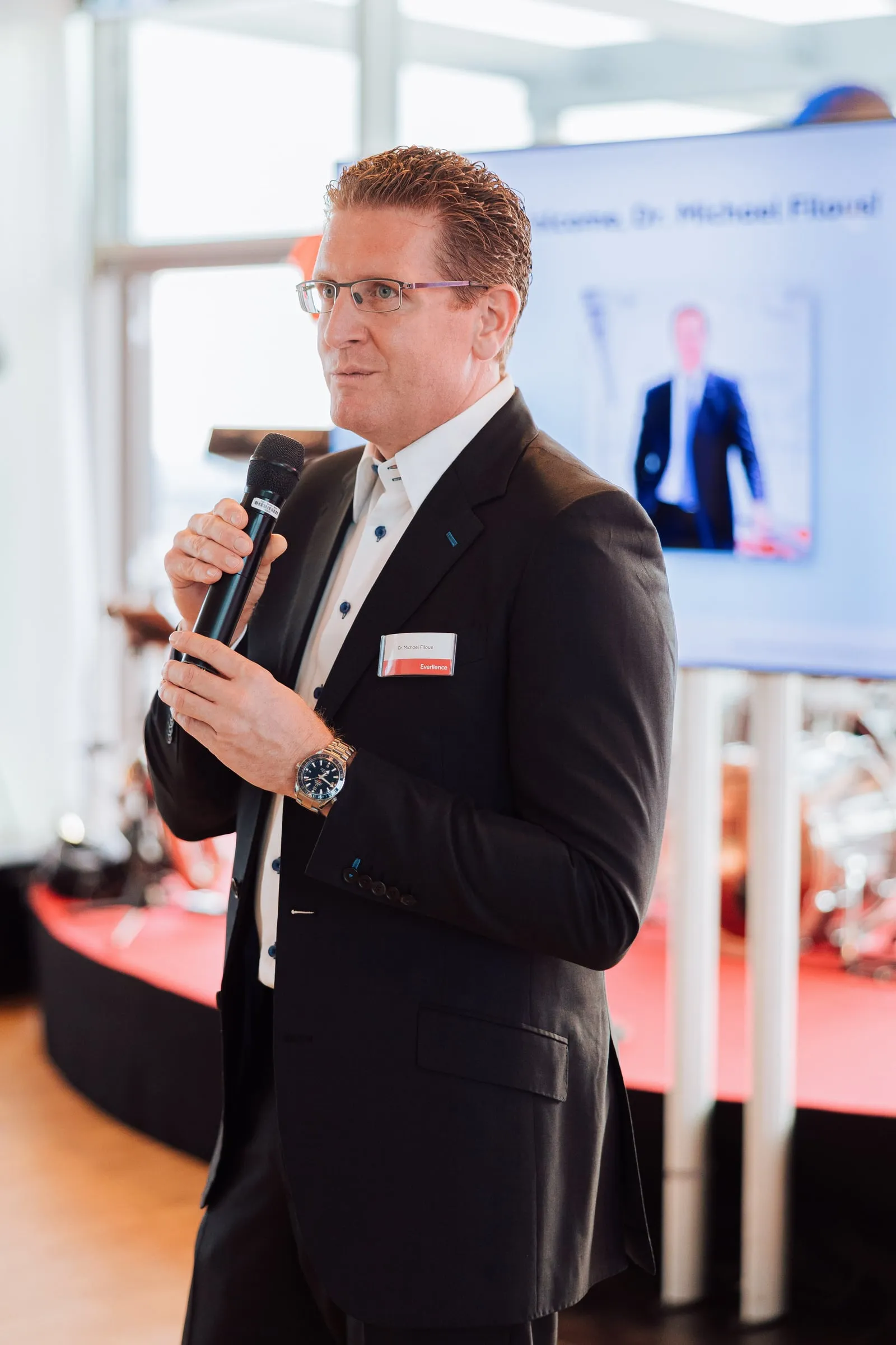 Redner mit Mikrofon vor dem Screen.