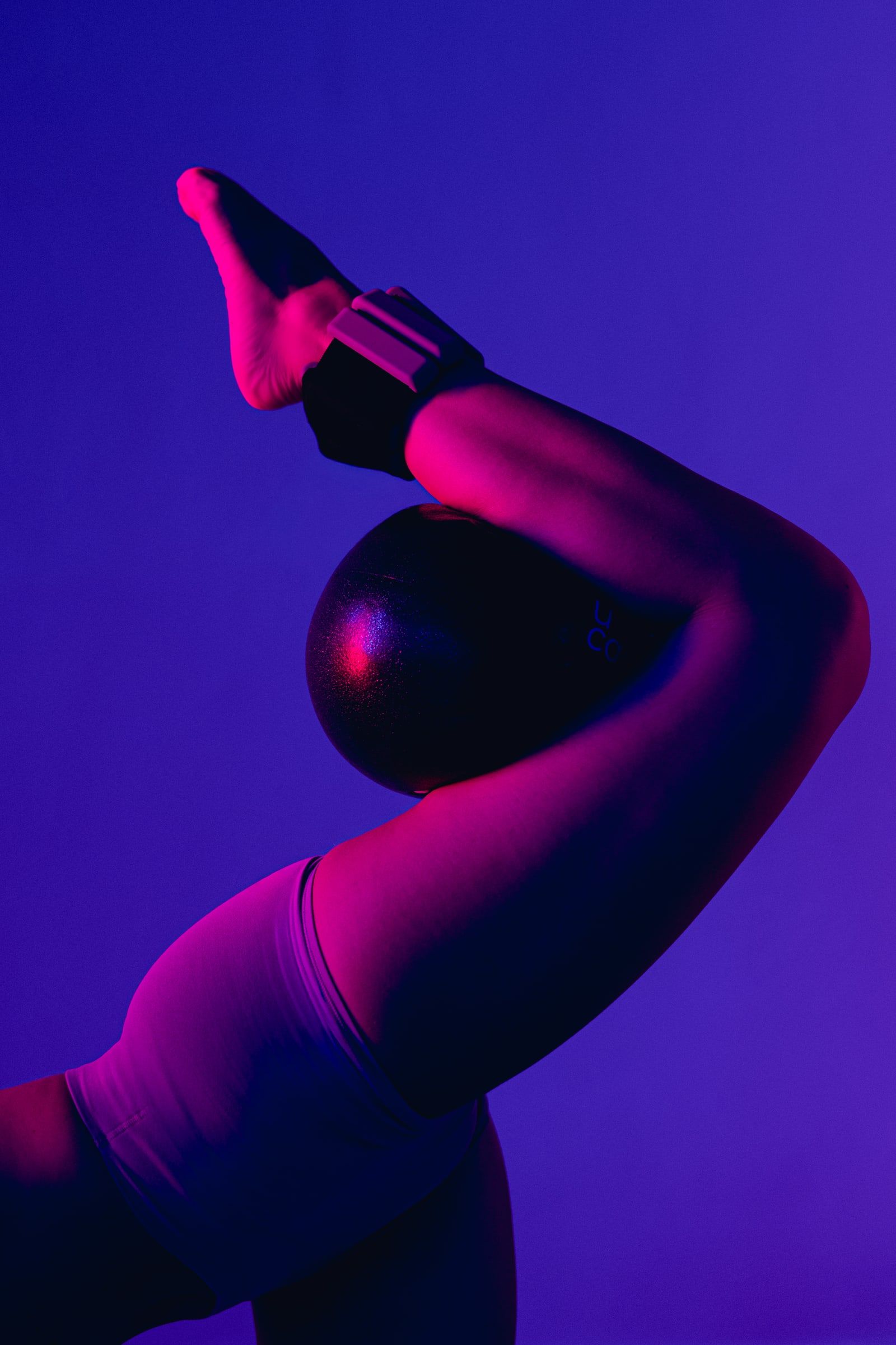 Bein mit Pilatesball in der Kniekehle im pinken Licht.