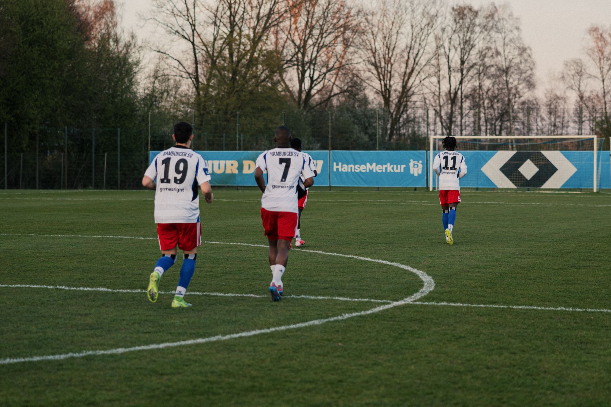Spieler in HSV-Trikots laufen im Abendlicht über den Trainingsplatz.