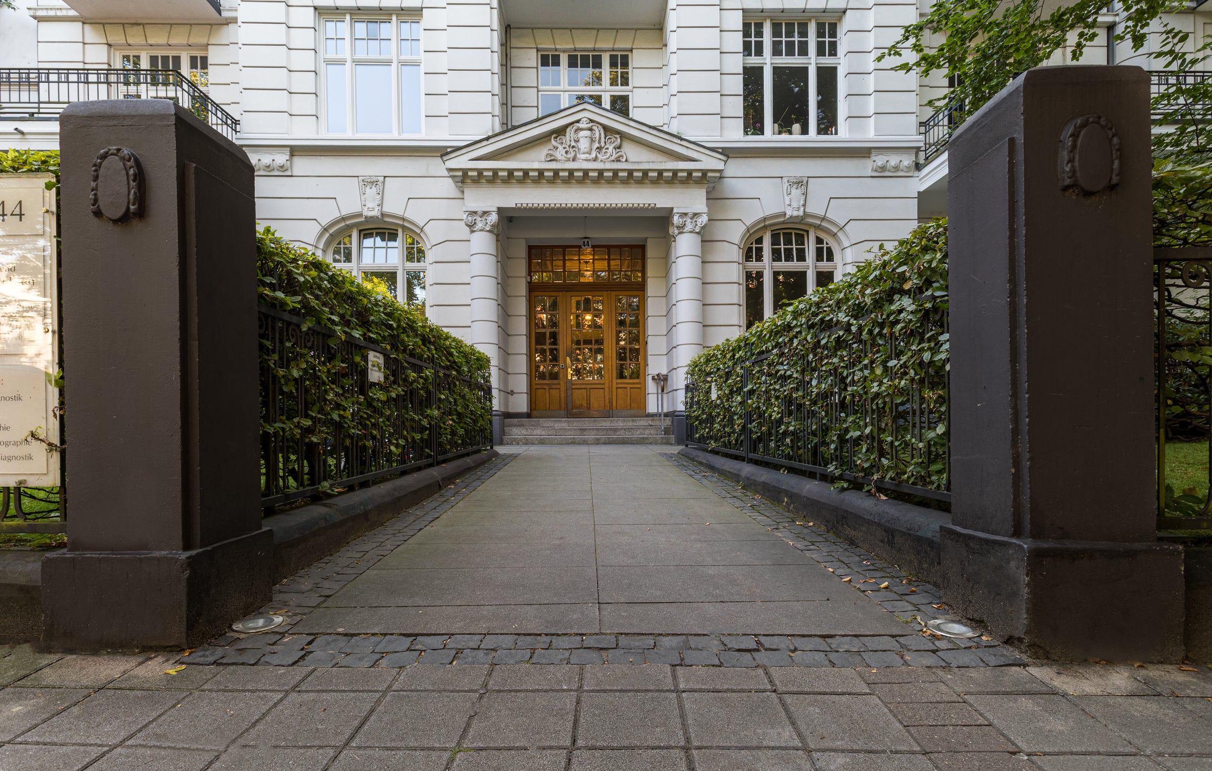 Zugang zum Altbau zwischen Hecken.