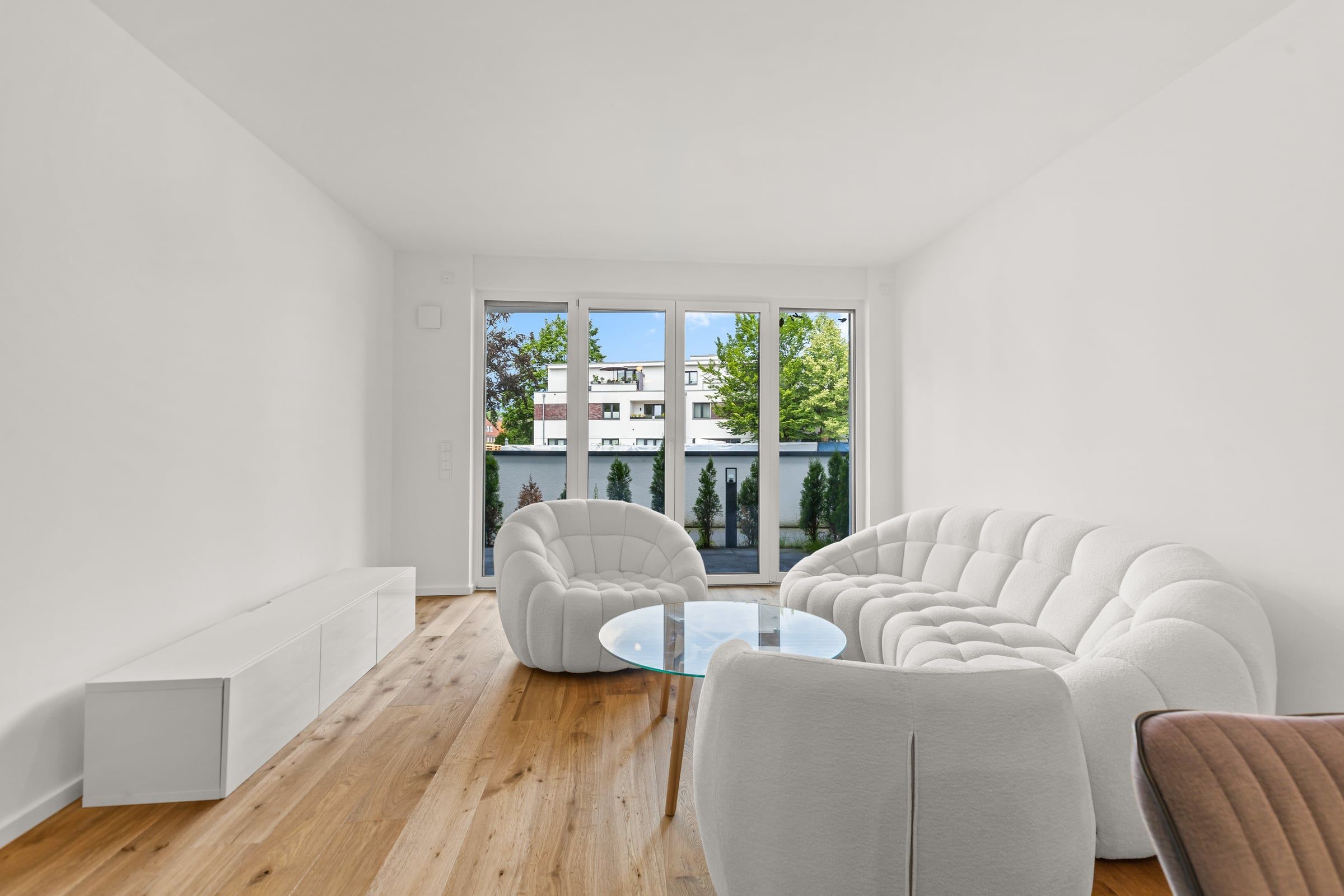Heller Wohnraum mit weißen Sofas und bodentiefen Fenstern.