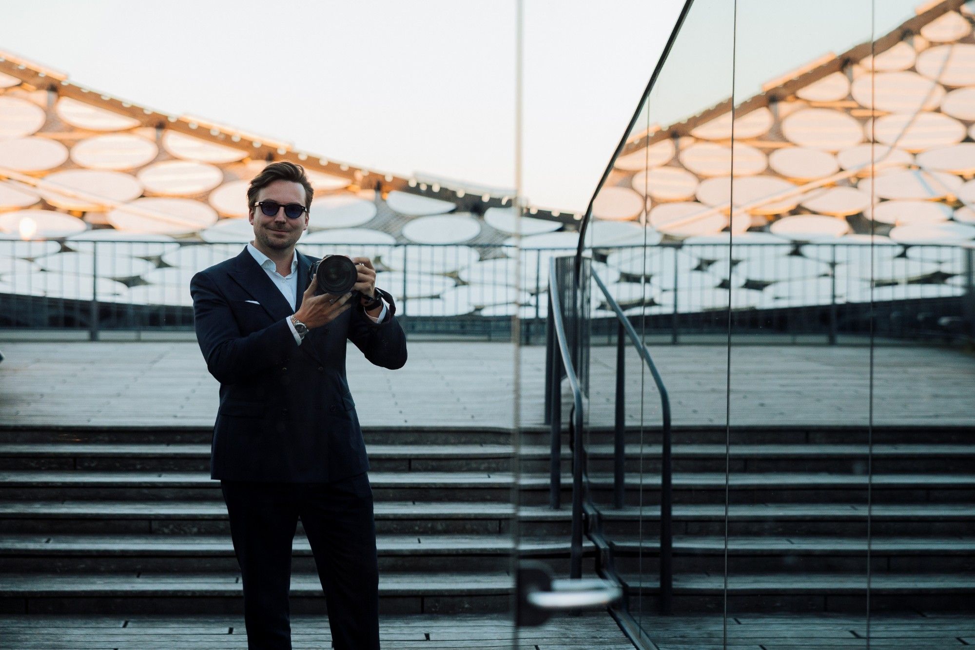 Marcel Kuhls mit Kamera auf der Plaza der Elbphilharmonie, gespiegelt in einer Glasfront.
