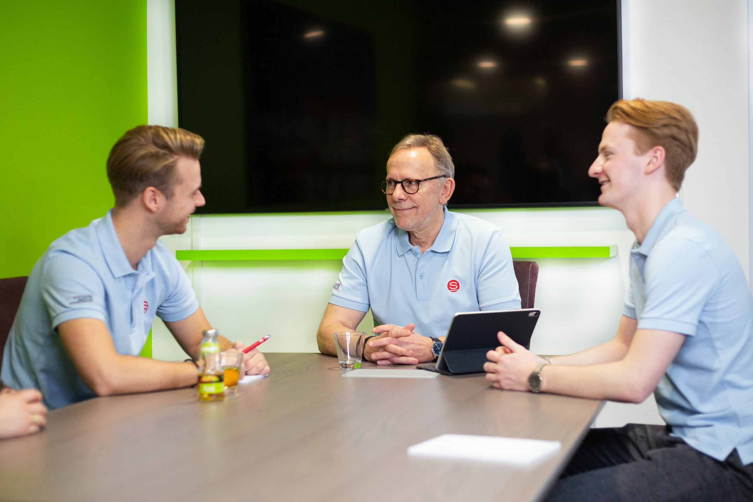 Drei Kollegen von Stadermann lachen im Gespräch am Besprechungstisch.