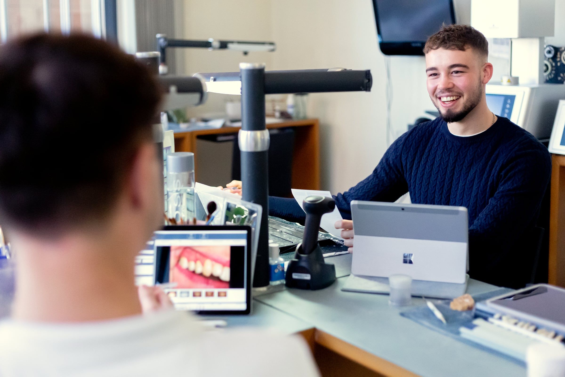 Zahntechniker lacht am Arbeitsplatz mit DENTAplus.