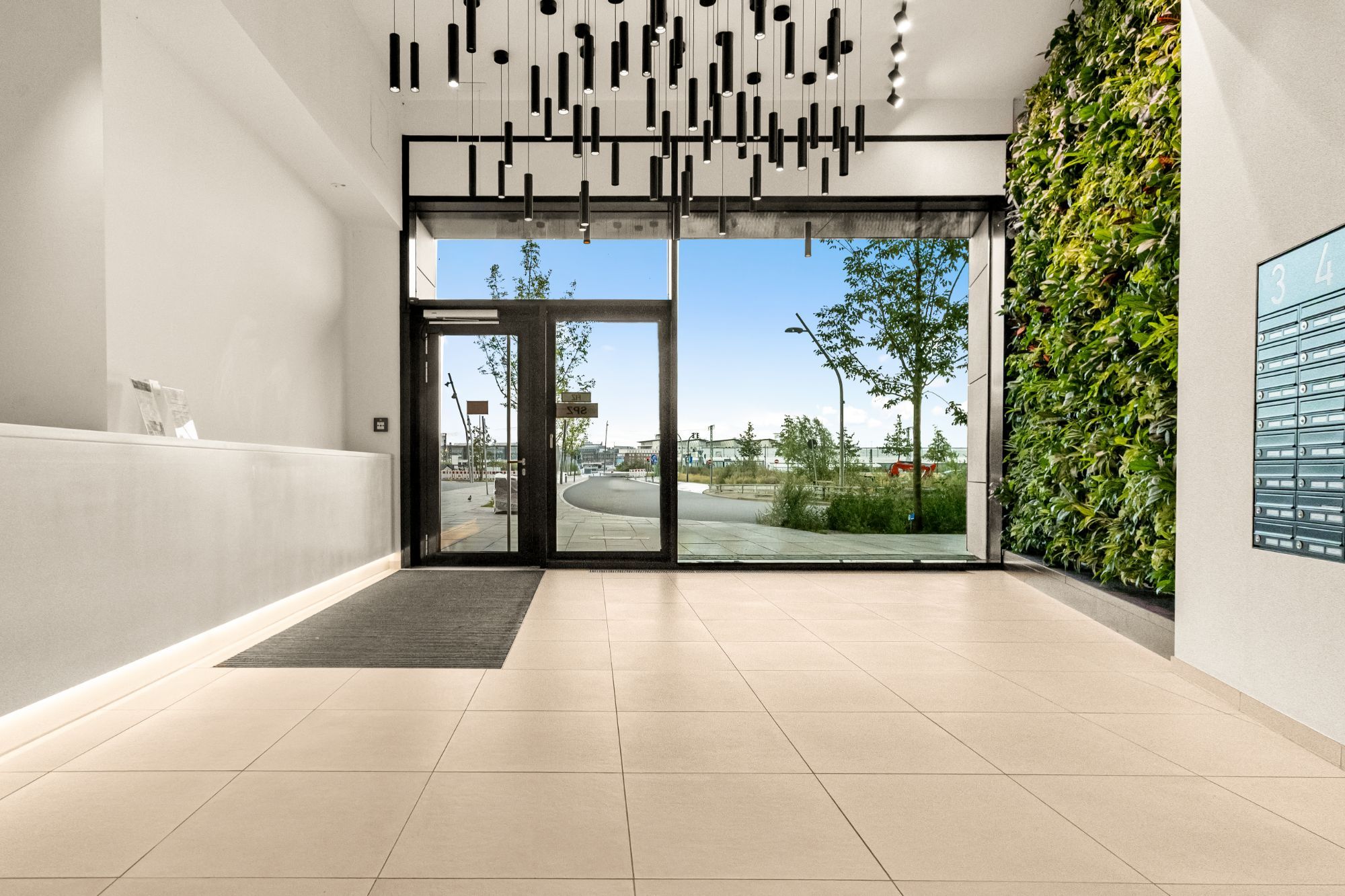 Eingangshalle mit schwarzen Pendelleuchten, bepflanzter Wand und großer Glasfront.