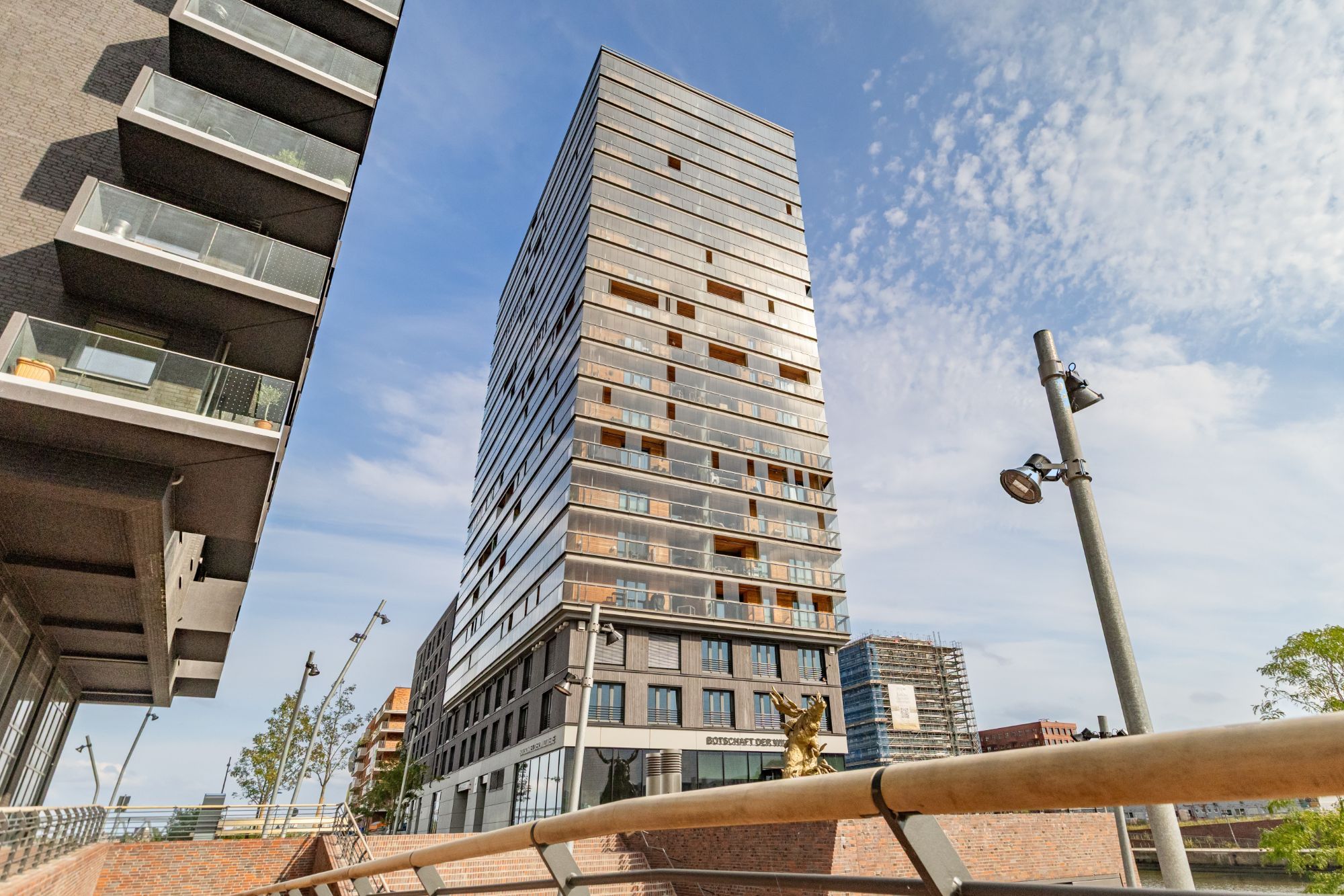 Wohnhochhaus mit Glasfassade und Loggien vor blauem Himmel.